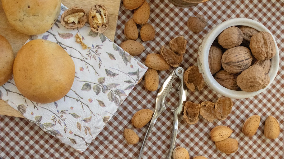 A delicious flat lay of bread rolls, walnuts, and almonds on a checkered tablecloth.