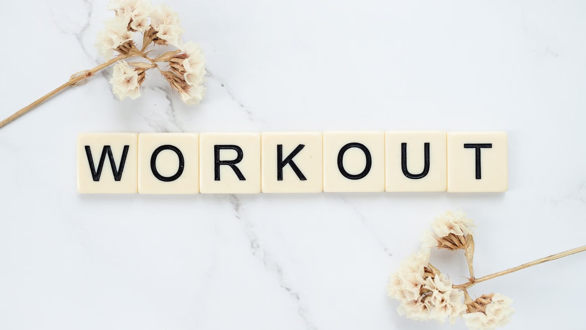 Letter tiles spelling 'WORKOUT' on marble with dried flowers, conveying fitness motivation.